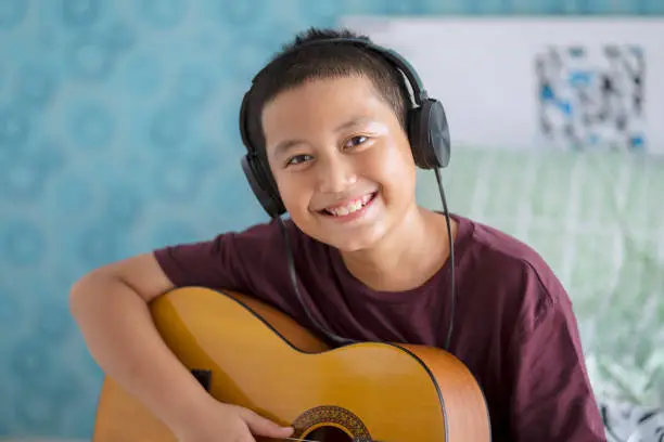 Portrait of a cute little boy wearing headset while playing acoustic guitar. Shot at home