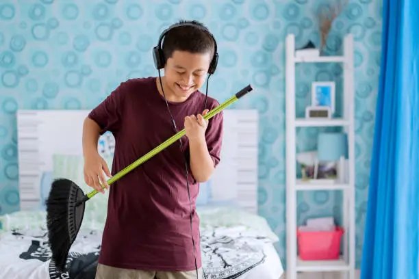 Picture of adorable little boy playing guitar with a broom while wearing headset. Shot in the bedroom