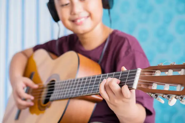 Closeup of little boy playing acoustic guitar while wearing headset. Shot at home