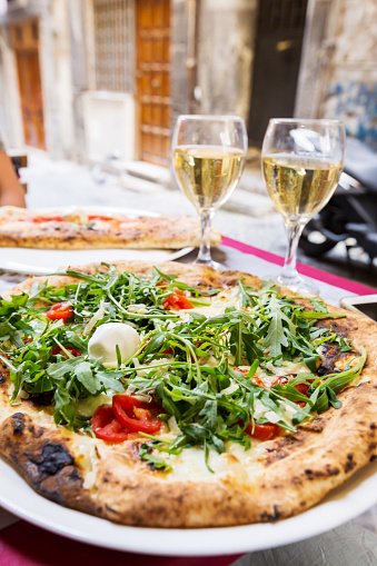 Italian pizza with arugula, tomato and cheese on the table in a restaurant outside over blurred background