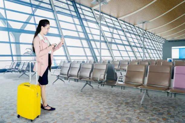 Picture of young businesswoman using a digital tablet while standing with a luggage in the airport lounge