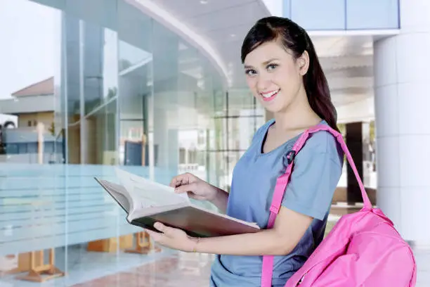 Image of Caucasian female college student smiling at the camera while holding a textbook