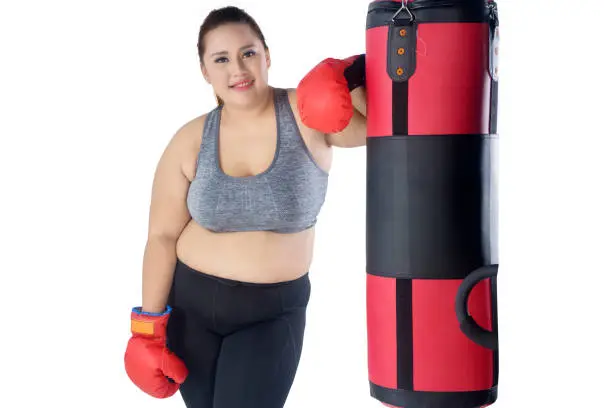 Picture of beautiful fat woman smiling at the camera while leaning on a bag boxing, isolated on white background