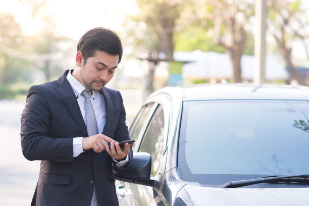 istock Handsome businessman using a mobile phone lerning on his car 1014888648