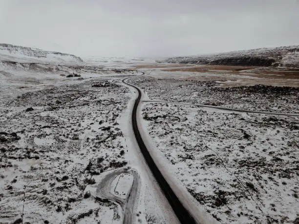 A curvy road in Iceland going through a snowy landscape, shot with a drone