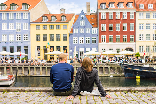 Copenhagen, Denmark - July 7, 2017. Tourists enjoying the scenic summer view of Nyhavn pier. Colorful building facades with boats and yachts in the Old Town of Copenhagen, Denmark