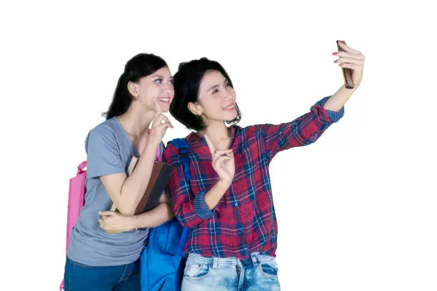 Picture of two college students using a smartphone to take a selfie photo together, isolated on white background