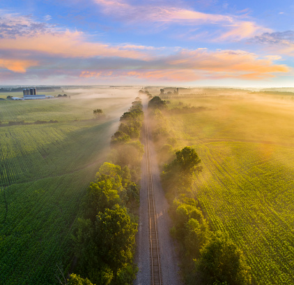 Foggy rural landscape with railroad tracks at sunrise, aerial view.
