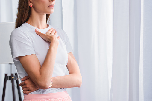 cropped image of worried woman with hand on chest in front of curtains at home