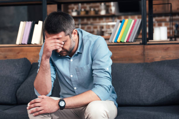 istock depressed man with hand on forehead sitting on sofa in psychiatrist office 1014934636