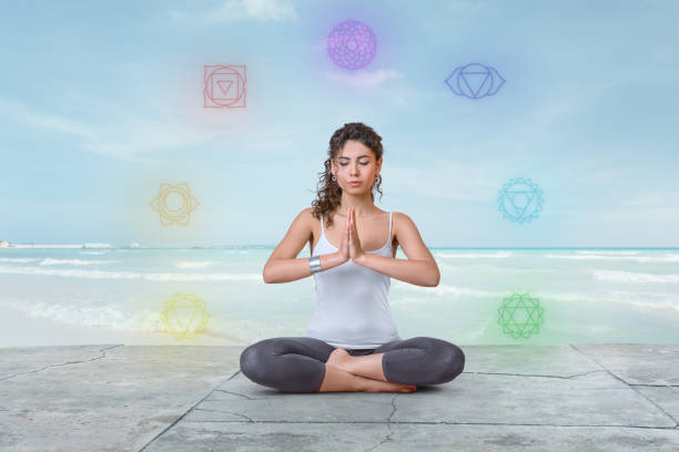 Young woman is meditating on the beach with chakras glowing around her stock photo