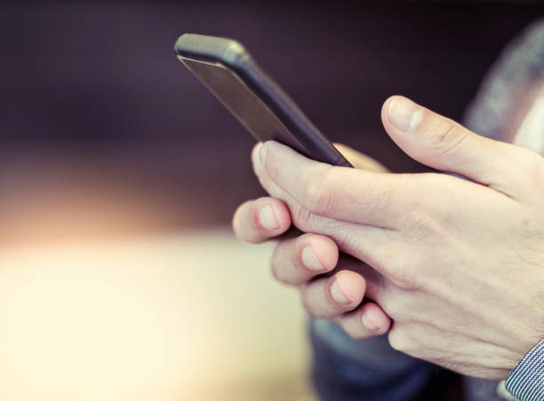 istock Male hands holding mobile phone and texting with defocused background 1014962072