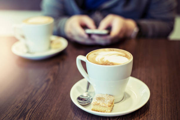 istock Two cappuccinos and background man using mobile phone 1014963760