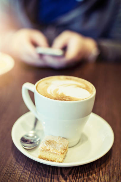 istock Cappuccino and cookie, man behind using phone 1014964120