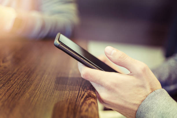 istock Male hand holding mobile phone by wooden table 1014966016