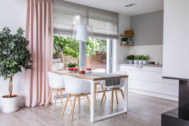gray roman shades and a pink curtain on big, glass windows in a modern kitchen and dining room interior with a wooden table and white chairs - shade imagens e fotografias de stock