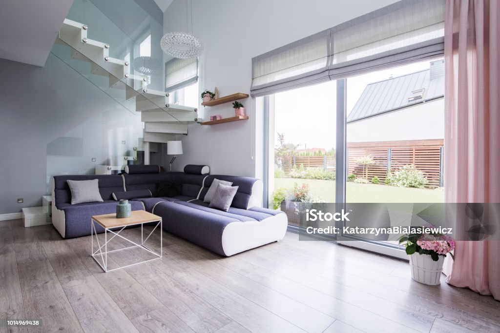Natural light coming through big glass door to a monochromatic, open space living room interior with a modern sofa on hardwood floor Shade Stock Photo
