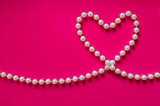 White pearl heart on a bright pink background. Pearl beads in the shape of heart. Glamorous background for processing