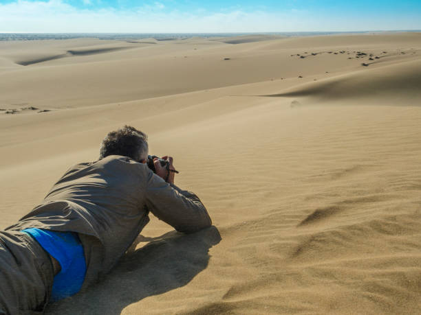 Man taking pictures on desert Photographer taking some pictures of the dunes over the sand tecnología inalámbrica stock pictures, royalty-free photos & images