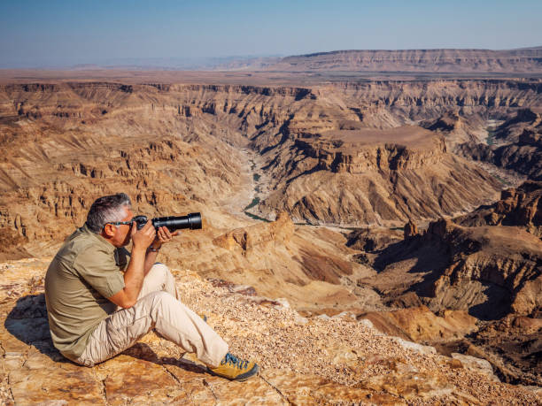 Man taking pictures on desert Photographer taking some pictures of the Fish River Canyon tecnología inalámbrica stock pictures, royalty-free photos & images