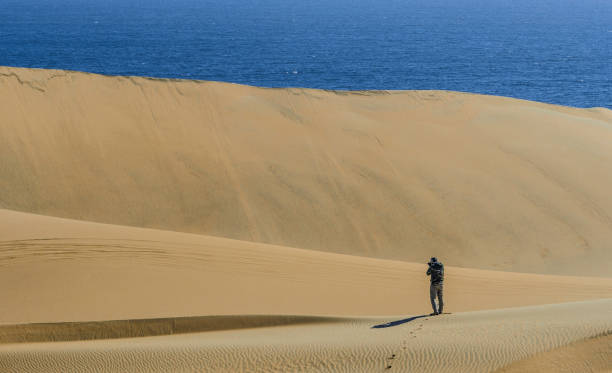 Man taking pictures between dunes Photographer taking some pictures of dunes of desert close to the ocean tecnología inalámbrica stock pictures, royalty-free photos & images