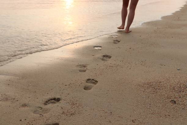 istock A women walking on the beach at sunset and leaving footprints behind. This image can be used to represent solo travel. 1014998280