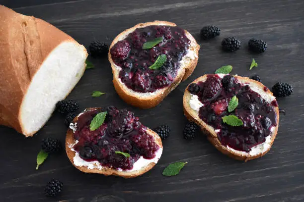 Slices of toast topped with goat cheese, blackberry compote, and mint leaves
