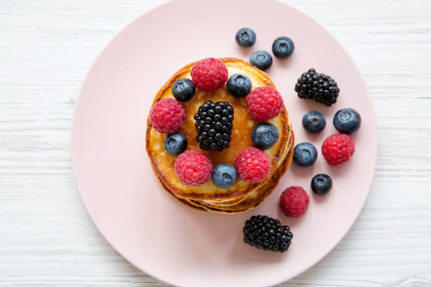 istock Pancakes with berries on a pink plate over white wooden table, top view. 1015042218