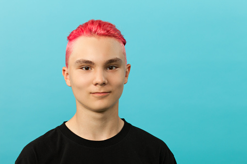Retrato de un muchacho adolescente con cabello rosado en el estudio sobre un fondo azul photo