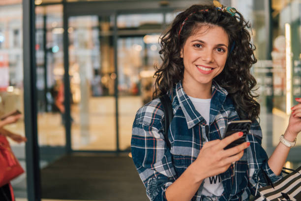 istock Young woman using mobile phone while exiting shopping mall 1015072612