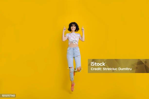 Cheerful Woman Jumping And Pointing Up Stock Photo - Download Image Now - Women, People, Colored Background