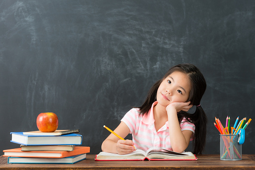 smiling young little girl writing education homework and daydreaming prepare back to school when she studying in blackboard background.