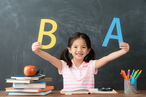 cheerful pretty female student back to school studying and sitting in blackboard background face to camera showing english word.