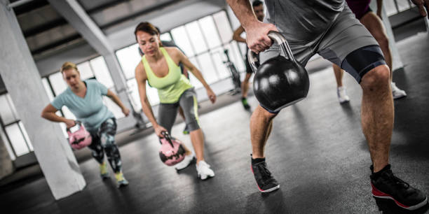 Group of people in the gym in a fitness class doing lunges with kettlebells. Instructor in the foreground.