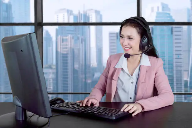 Beautiful customer service working with headphone and computer while sitting near the window