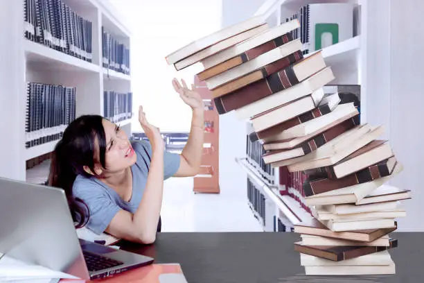 Image of female college student holds falling books while studying and sitting in the library