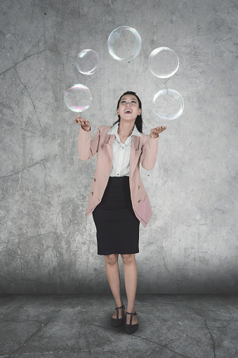 Full length of Caucasian businesswoman juggling with soap bubbles while standing with happy expression