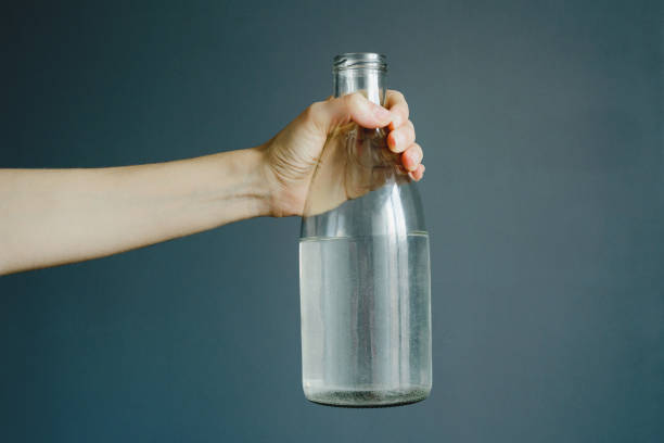 istock womans hand holds bottle with water on gray wall background 1015188706