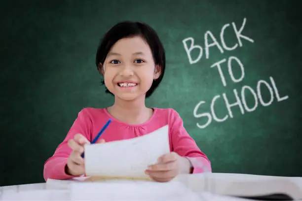 Picture of Asian cute schoolgirl smiling at the camera while learning to write in the classroom with text of back to school