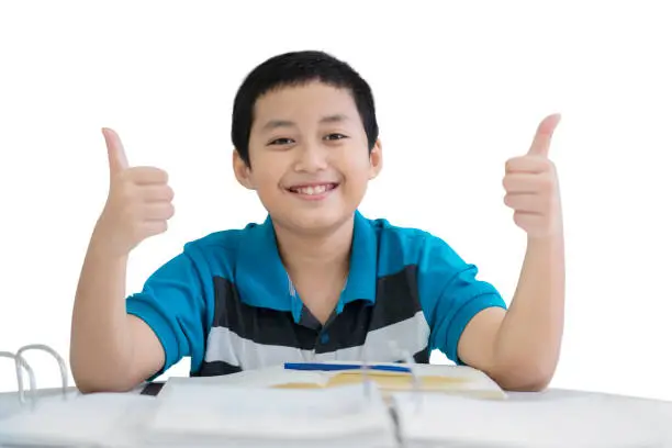 Image of little boy showing thumbs up at the camera while studying in the studio, isolated on white background