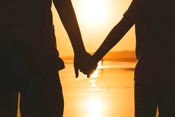 Close up of two children holding hands while walking on the beach. Shot at sunset time