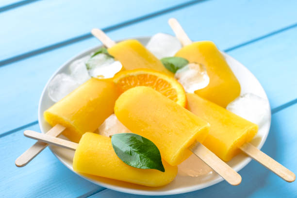 istock Orange popsicle on blue wooden background. Summer refreshing ice on stick. 1015214746
