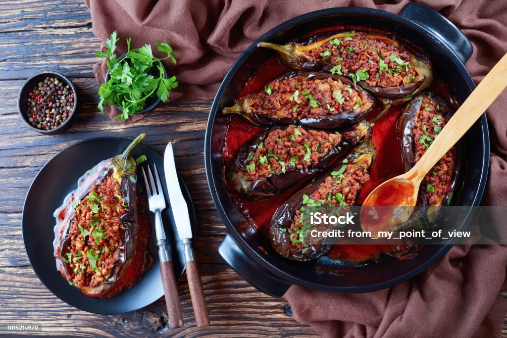 Karniyarik - Stuffed Eggplants on a plate Karniyarik - Stuffed Eggplants, Aubergines with ground beef and vegetables baked with tomato sauce served on a plate with fork and knife, turkish cuisine, horizontal view from above, close-up, flatlay Eggplant Stock Photo