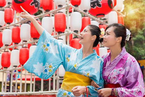 beautiful young female travelers standing in front of celebration lantern decorations and pointing local landscape when they travel in japan with traditional kimono.