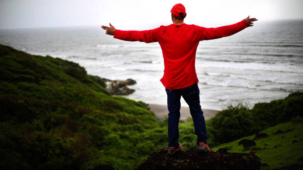 Freedom in the nature Young happy Indian men wearing red color t-shirt and blue jeans standing on rock and doing hand raised freedom concept and enjoying fresh air outdoors in the nature. chapora fort stock pictures, royalty-free photos & images