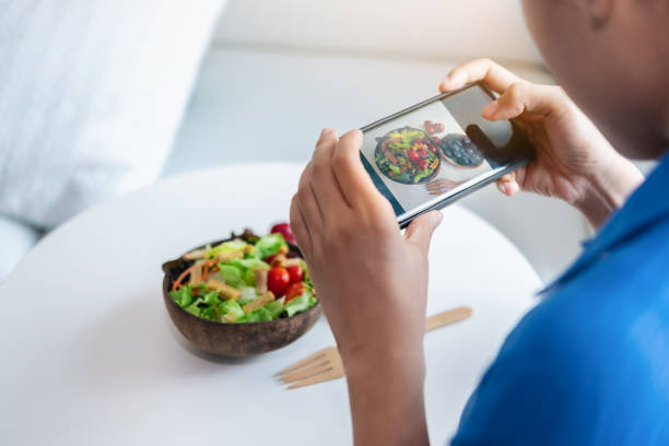 A woman is using smartphones to take photos to post a salad she made in her social. stock photo