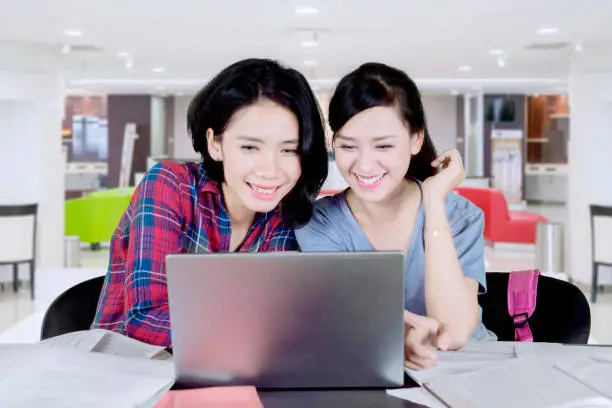 Image of Asian girl using a laptop and doing homework with her friend in the canteen
