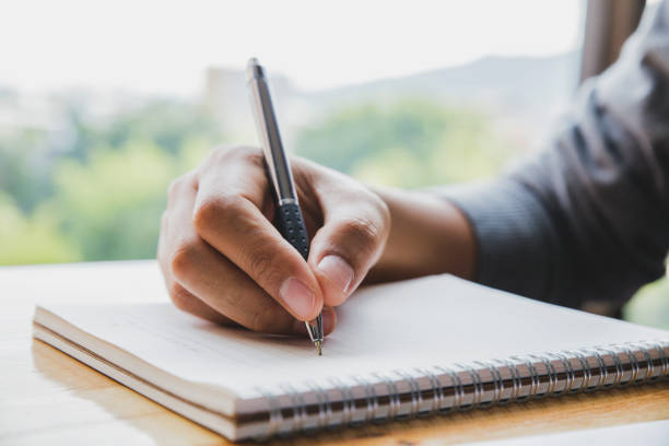 istock Close up image of man hand writing on notebook with wooden table background 1015250054