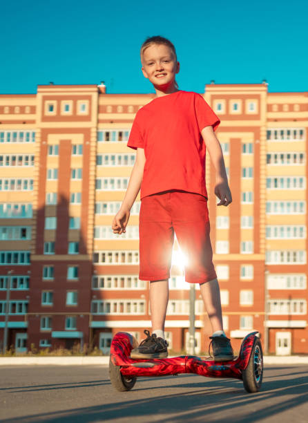 Cheerful Boy is Riding on Self-balance Scooter A happy preadolescent age boy dressed in a casual clothing in a city scatepark. He rides on the hoverboard. The boy smiling looking at camera. Outdoors shooting on a summer sunset hoverboard stock pictures, royalty-free photos & images
