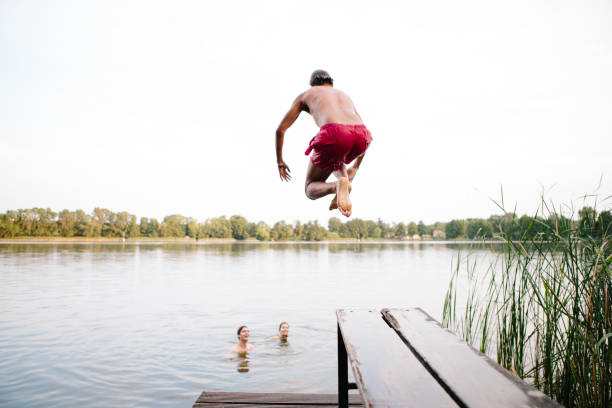 istock Summer day: three young adults jump from jetty into lake 1015255644